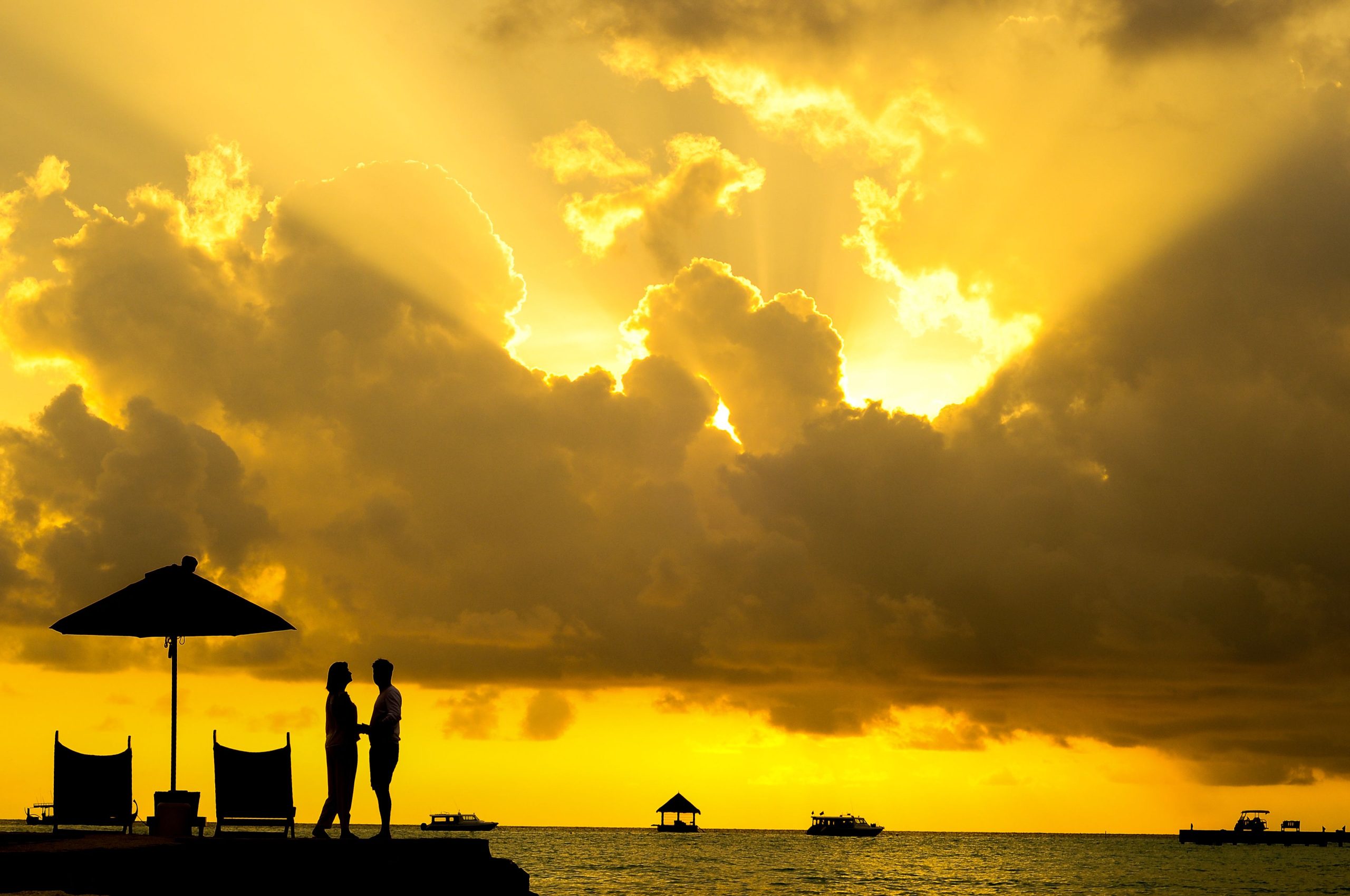 Silhouette of a couple sharing a romantic kiss beneath a vibrant tropical sunset, symbolizing the idealized fantasy romance we often imagine