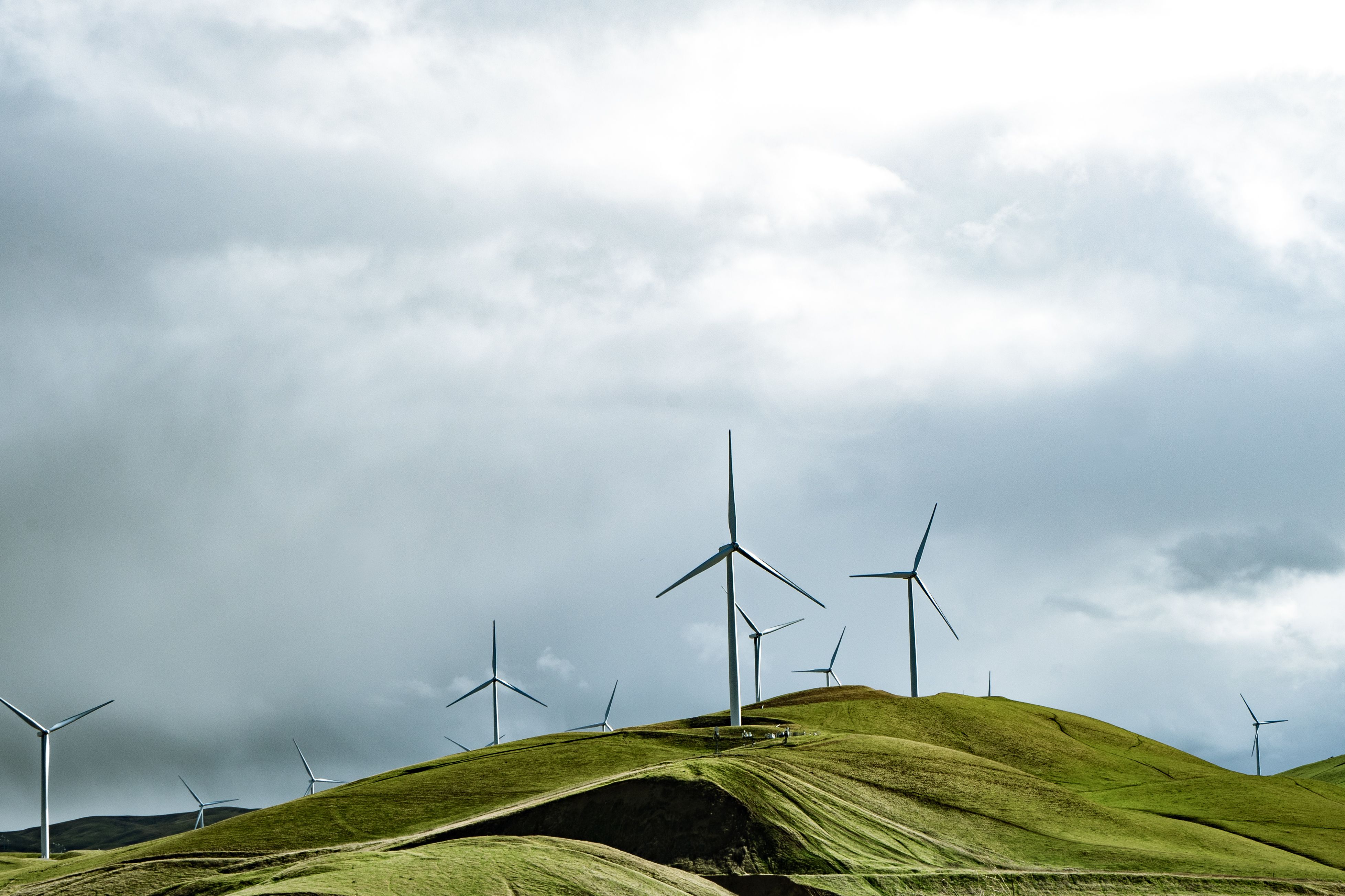 Wind turbines on green hills beneath a dramatic sky, representing renewable energy development and compliance planning.