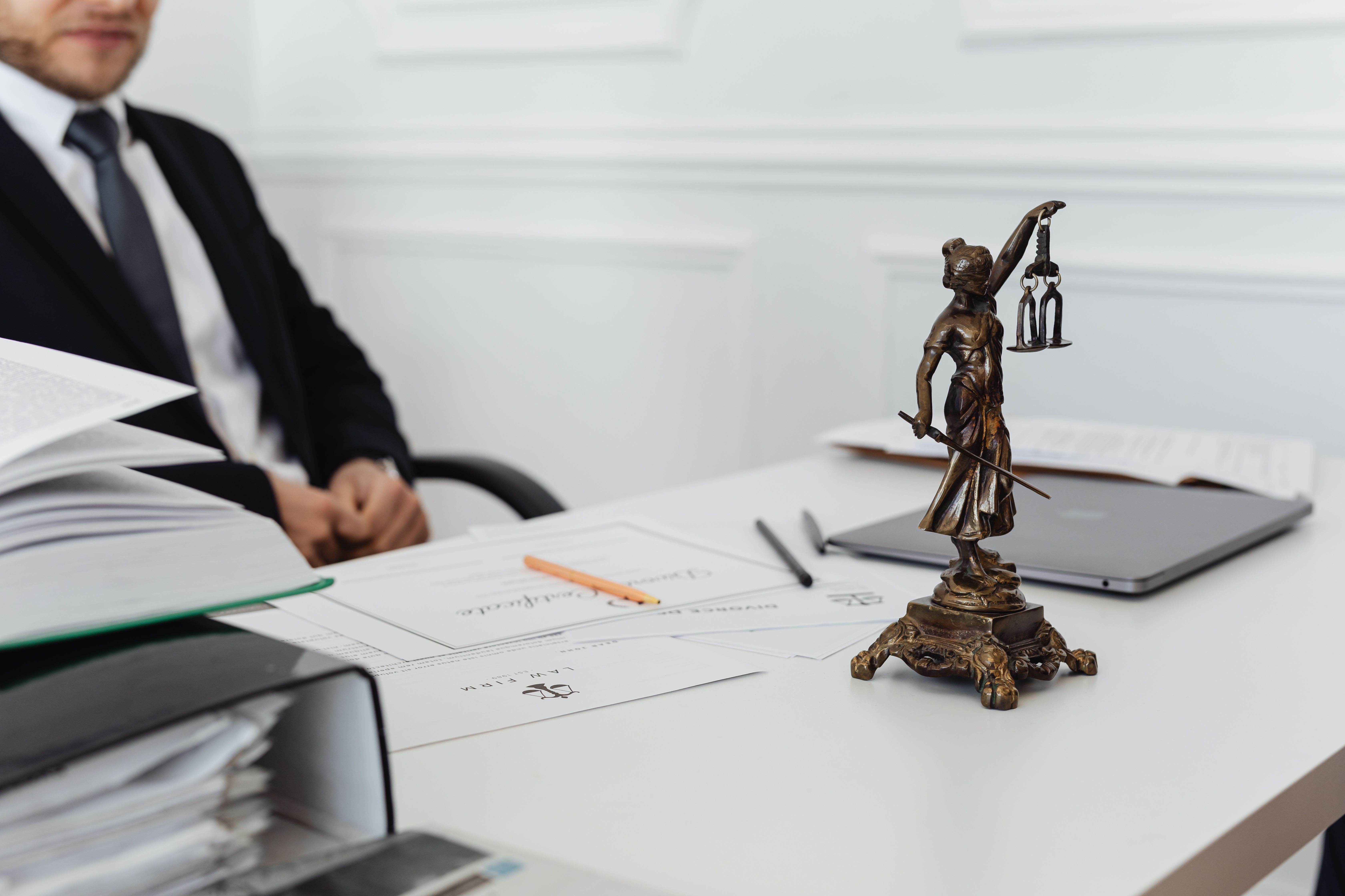 Legal professional's workspace with a Lady Justice statue, case documents and a laptop representing the review of a new client's file