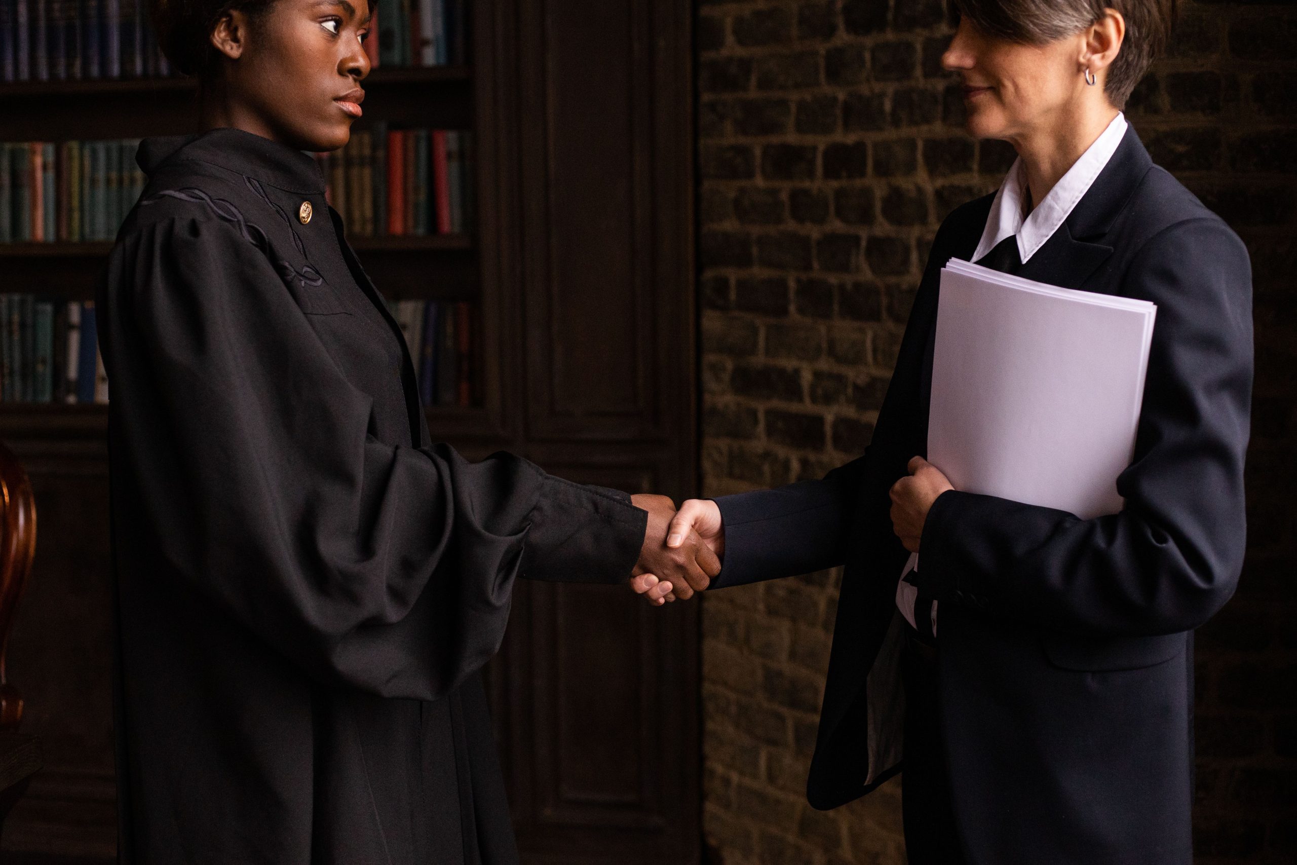 Attorney in formal attire shaking hands with a new client in a book-lined law office, marking the start of a new legal representation